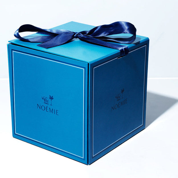 Blue gift box with a blue ribbon and 'Noémie' branding on a white background