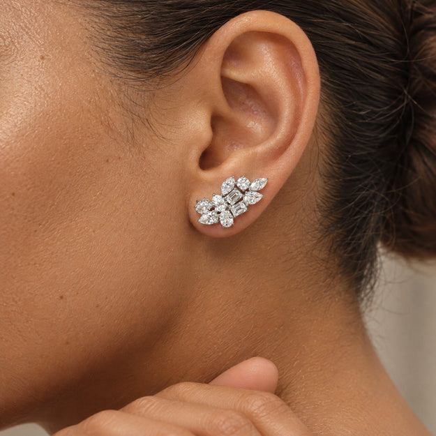 A close-up of a woman's ear wearing a silver-toned stud earring with a floral cluster of clear gemstones.