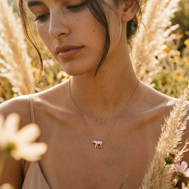 Woman wearing a necklace with a small animal pendant in a natural setting with flowers and plants.