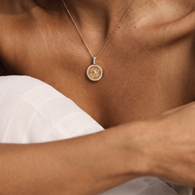 A close-up of a person wearing a delicate gold pendant necklace with a circular star design, styled with a white top.
