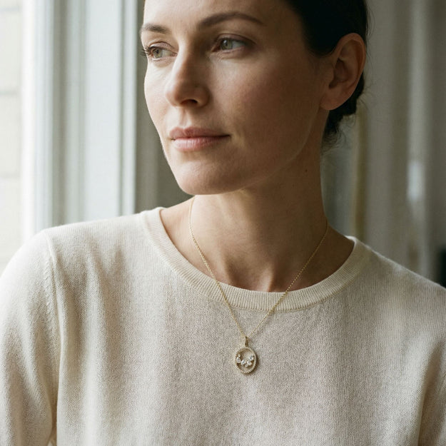 Woman wearing a beige sweater and necklace with a neutral background