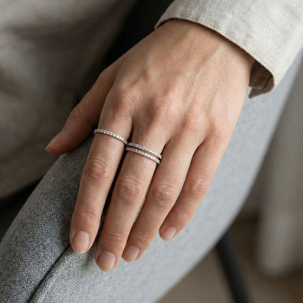 Hand wearing two silver rings on a neutral background