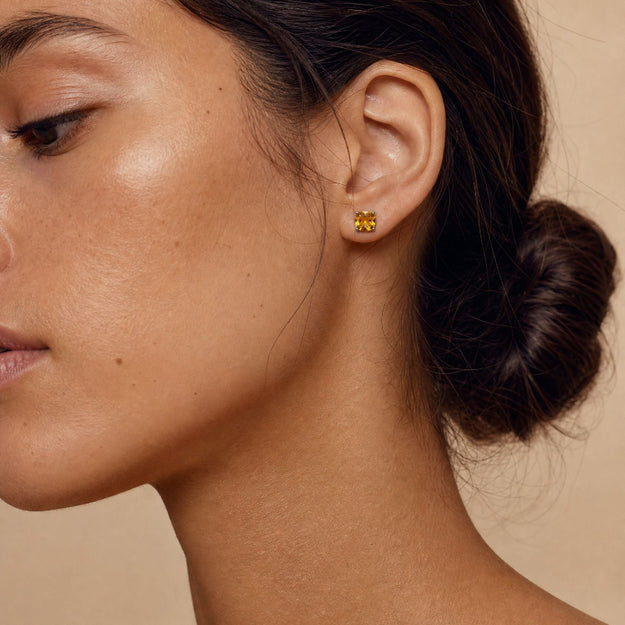 Close-up of a person wearing gold earrings with a neutral background