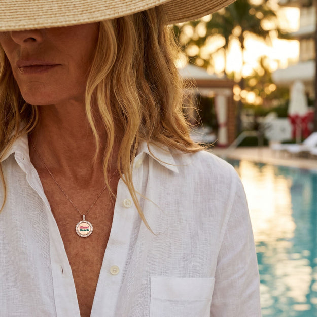 Person wearing a straw hat and white shirt with a visible brand logo, standing by a poolside.