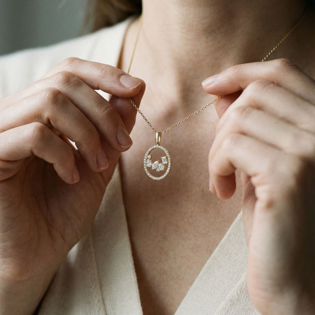 Person adjusting a delicate gold necklace with a small pendant.