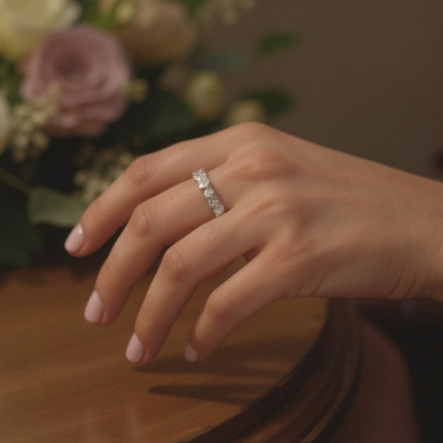 Hand wearing a diamond ring with a bouquet of flowers in the background
